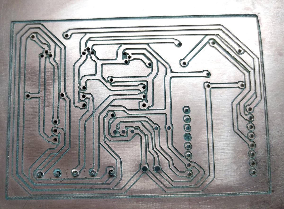 PCB recién fresada sobre la bancada de la CNC: pistas de cobre visibles, taladros limpios