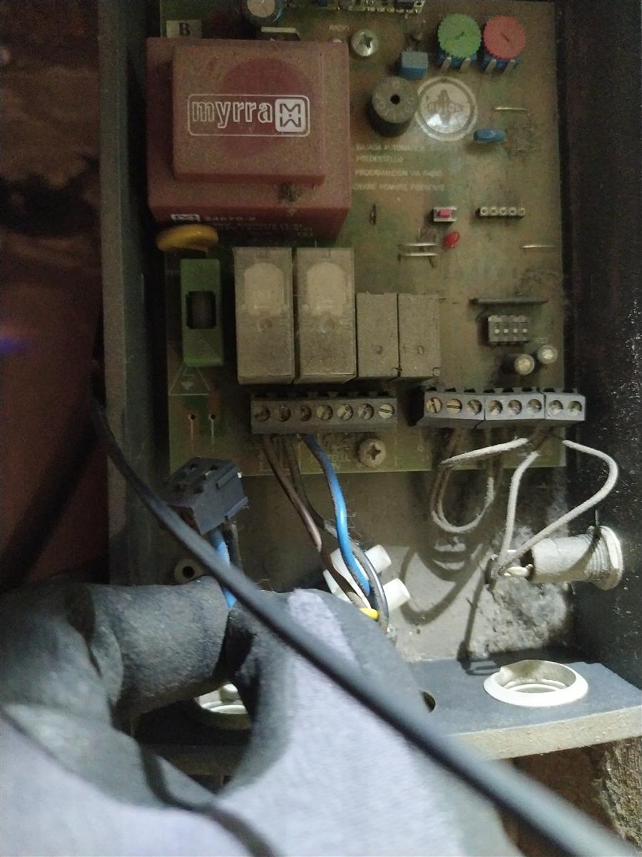 Placa controladora Myrra de persiana motorizada abierta: transformador rojo Myrra arriba a la izquierda, tres relés en el centro, regletas de bornes con cableado y el conector de entrada 220V desenchufado colgando en la parte inferior izquierda. Toda la placa cubierta de polvo acumulado en 30 años.