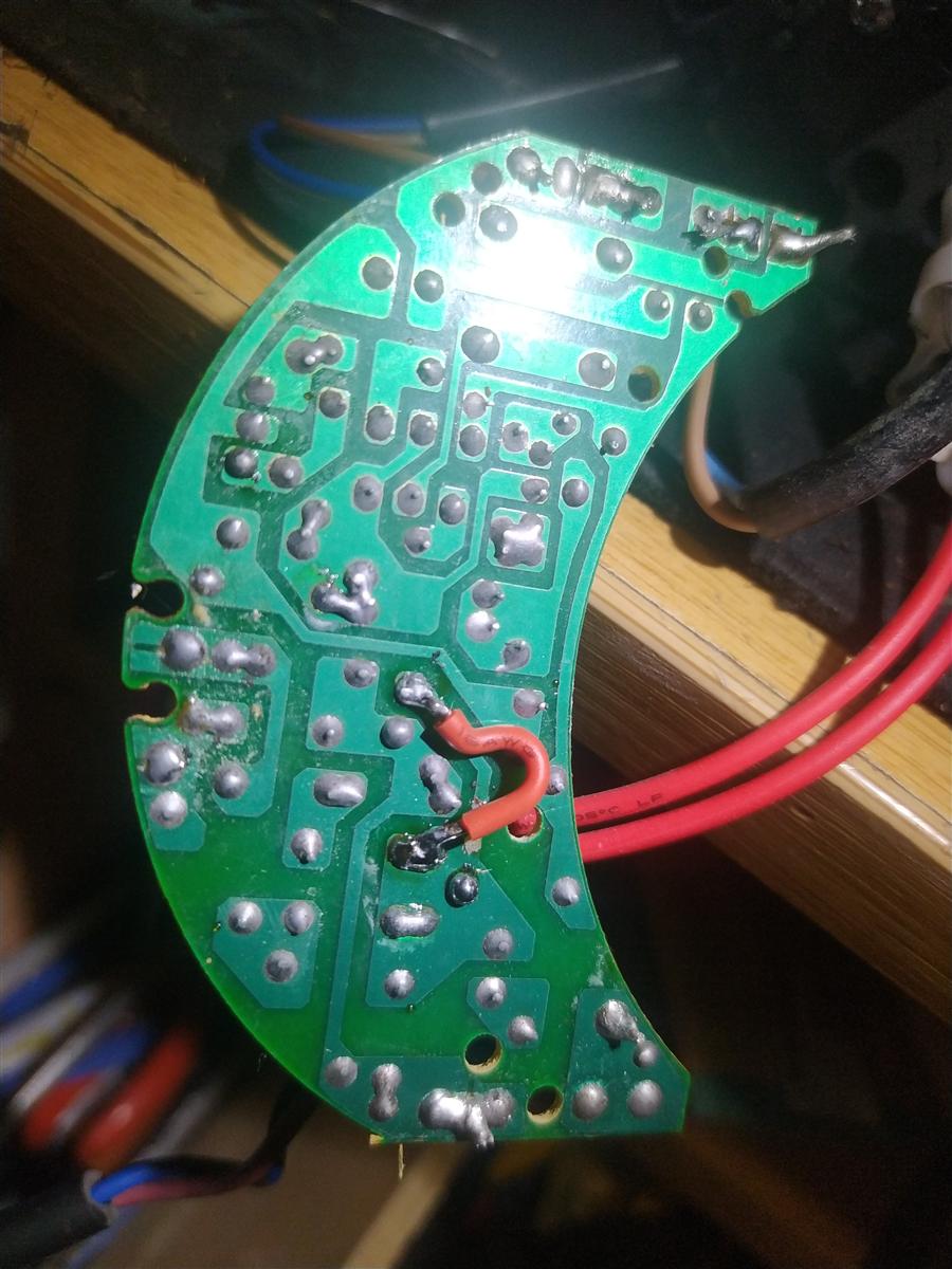 Parte trasera de la PCB semicircular del matamosquitos: múltiples puntos de soldadura y en el centro un puente de hilo rojo doblado en U soldado para puentear el contacto quemado
