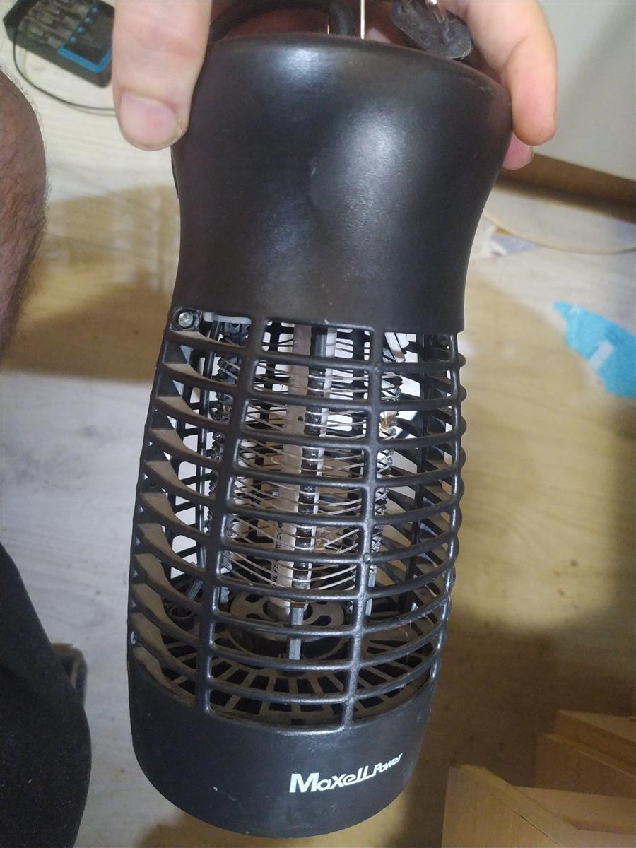 Matamosquitos MaxellPower MP-IK4W en mano: cuerpo cilíndrico de plástico negro con jaula de alambre alrededor de la lámpara UV y la marca MaxellPower serigrafiada en el lateral